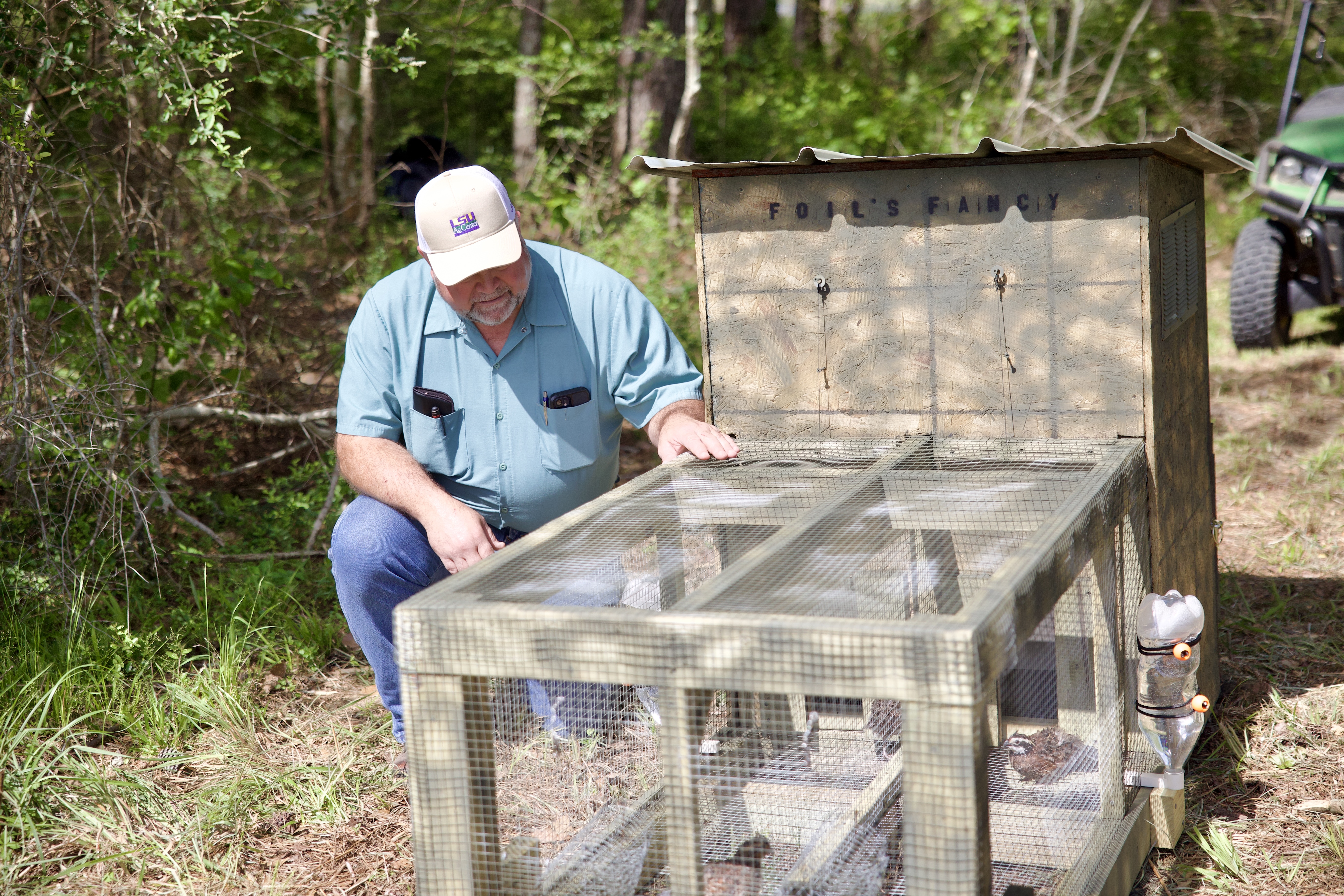 Jim LaCour kneeling next to a quail pen.